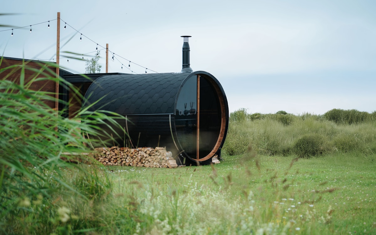 Black barrel sauna with glass front in a grassy backyard