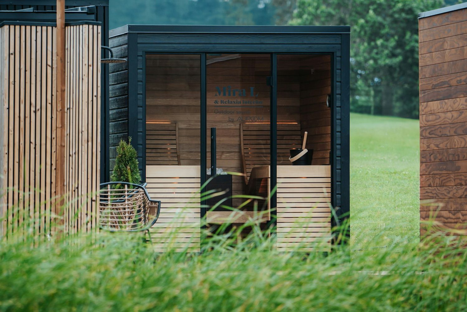 Modern black-framed outdoor cedar sauna with full glass front on a green residential lawn